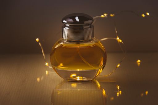 A closeup of a bottle of perfume with lights on it on the table against a blurry background