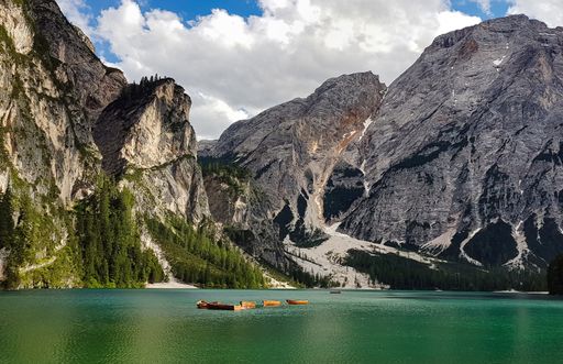 A beautiful shot of rocky mountains near a green pond under a bright cloudy sky