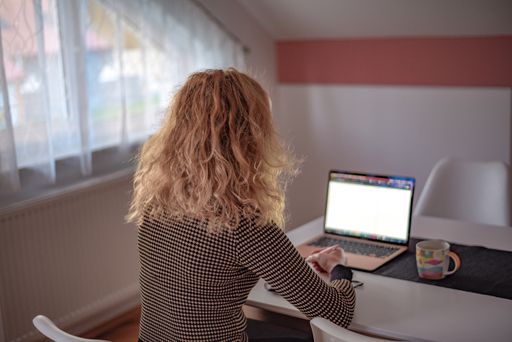 A rear view of a blonde woman near the desk working on her personal computer from home