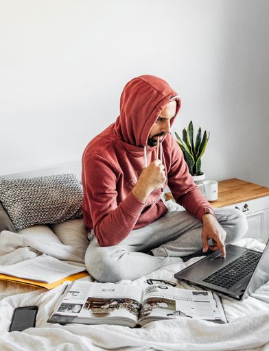 A vertical shot of a young male working on his laptop and studying on his bed