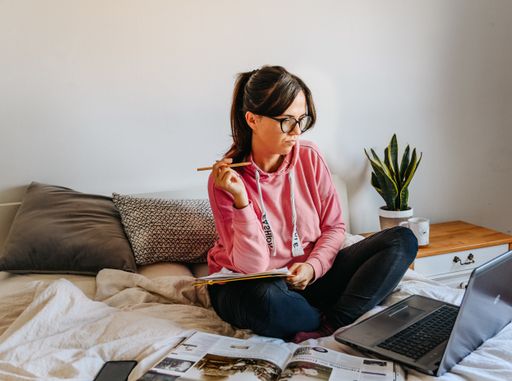 A young female student studying with her laptop and books on a bed