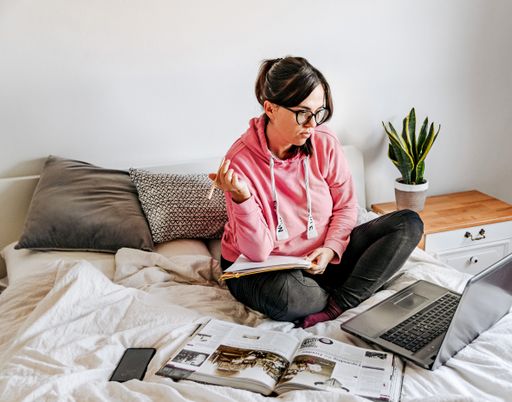 A caucasian female working with her laptop on a bed - work during the pandemic