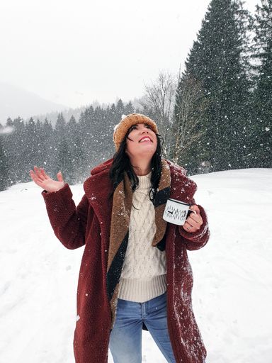 A young Caucasian female wearing a coat and drinking tea while enjoying the snow