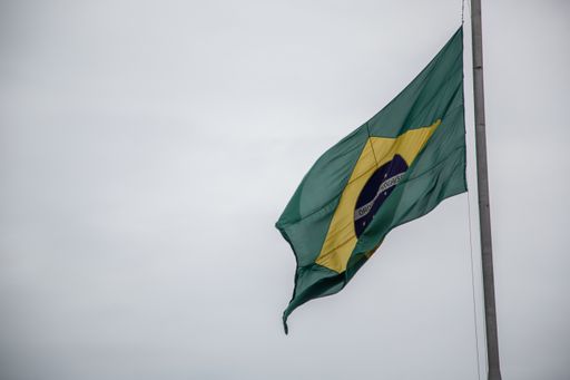 A low angle shot of the wavy flag of Brazil on a flagpole under a cloudy sky