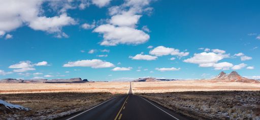 A beautiful scenery of a highway surrounded by fields under the cloudy sky