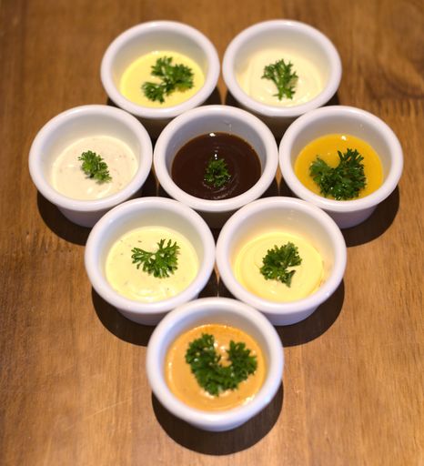 A top view closeup of different types of sauces in tiny white bowls with herbs on a wooden table