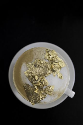 A vertical shot of a cup of cappuccino with a golden foam on black surface, luxury drink concept