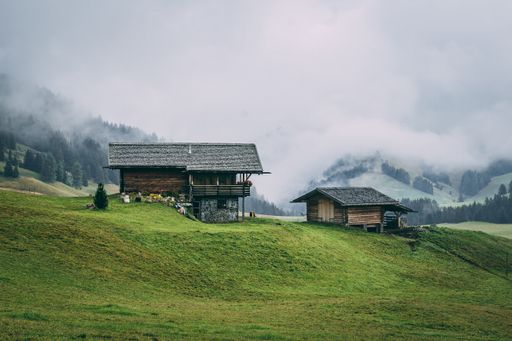 A rural area with wooden houses surrounded by forests with hills covered in the fog on the background