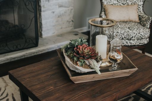 A wooden pot on a wooden table with flowers and candles on it near an armchair and a fireplace