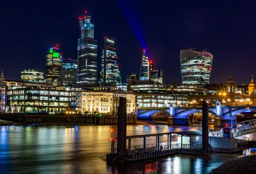 A picture of London with modern buildings and a bridge during the night with the city lights