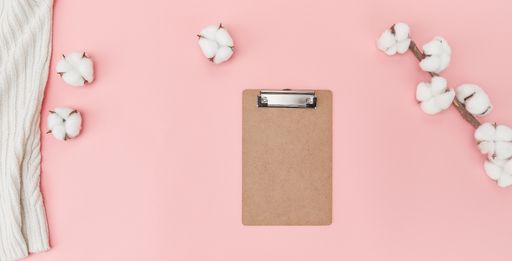 The flat lay of clipboard, towel, and cotton flowers with copy space on a pink surface
