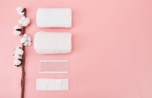 A high angle shot of cotton flowers, napkin, towels, and Qtips on a pink surface