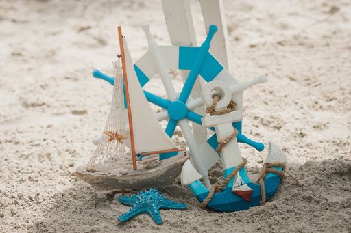 A small blue and white ship and anchor in a beach under sunlight with a blurry background