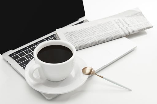 A high angle shot of a cup of coffee, laptop, and a newspaper on a white table indoors