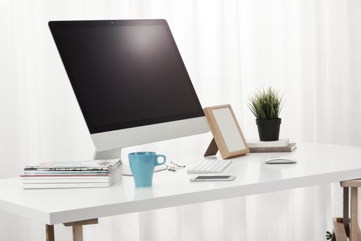 A closeup of a computer, a cup of coffee, books, magazines, and more on a white desk, indoors