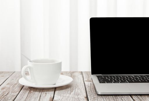 A closeup of a laptop and a cup of coffee on a wooden desk, indoors