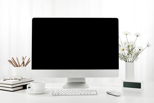 A closeup of a computer, a cup of coffee, a vase of flowers, and more on a white desk, indoors