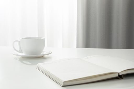 A closeup of a cup of coffee and a calendar notebook on a white desk, indoors
