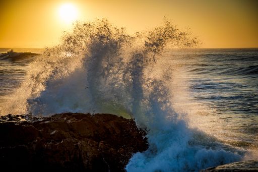 A view of sea waves breaking rocky beach during sunset