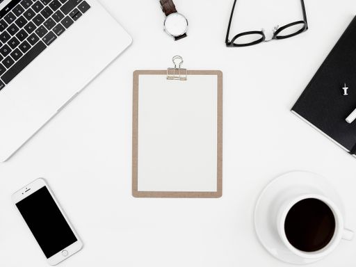A top view of a cup of coffee, paper, smartphone, laptop, and more on a white desk