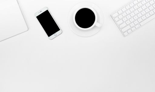 A top view of a cup of coffee, a smartphone, and a keyboard on a white desk
