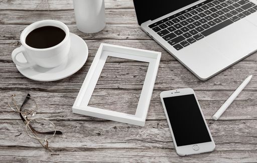 A high angle shot of a cup of coffee, laptop, notebook, a smartphone, a frame, and more on a wooden surface