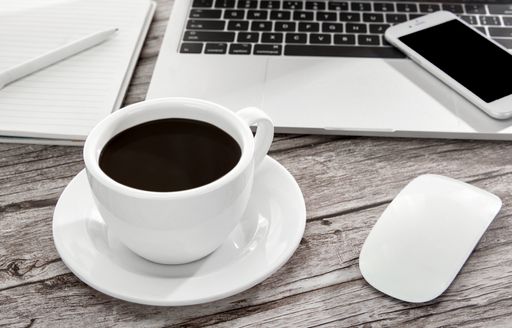 A high angle shot of a cup of coffee, laptop, notebook, a smartphone, and more on a wooden surface