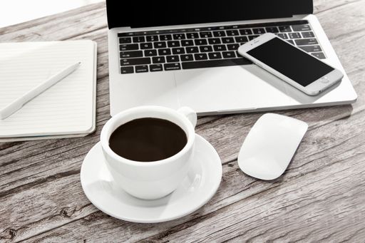 A high angle shot of a cup of coffee, laptop, notebook, a smartphone, and more on a wooden surface