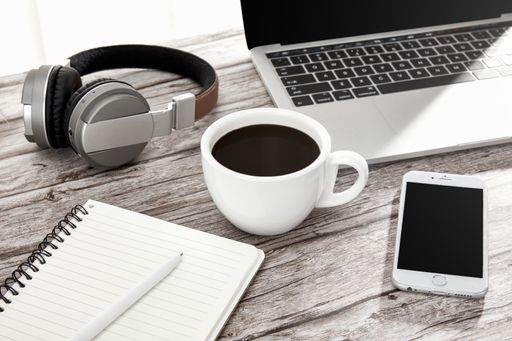A high angle shot of a cup of coffee, laptop, notebook, a smartphone, and headphones on a wooden surface