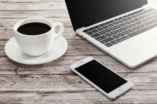 A high angle shot of a cup of coffee, laptop, and a smartphone on a wooden surface