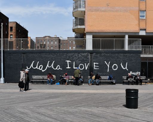 Mama I love you wall writing and graffiti, with people sitting in front of a black brick wall, on a wooden boardwalk in Brooklyn