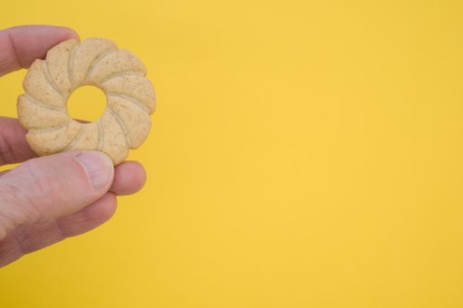 A closeup shot of a circle biscuit in a person's hand isolated on a yellow background