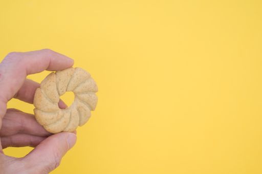 A hand holding a sun shaped cookie on yellow background with a copy space