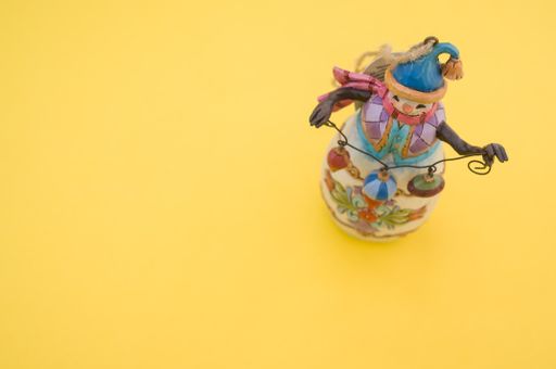 A high angle shot of a decorative handmade snowman isolated on a yellow background