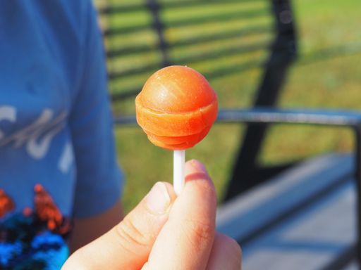 A selective focus shot of a boy's hand holding an orange lollipop