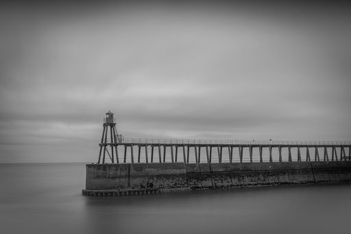 A pier at Whitby beach, UK in grayscale in cloudy weather