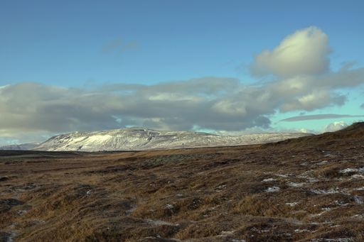 A landscape of a meadow surrounded by hills under a blue cloudy sky