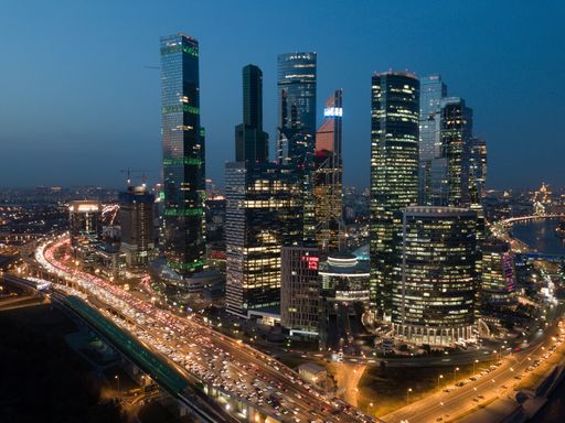 A cityscape of modern buildings with lights surrounded by water during the evening in Moscow
