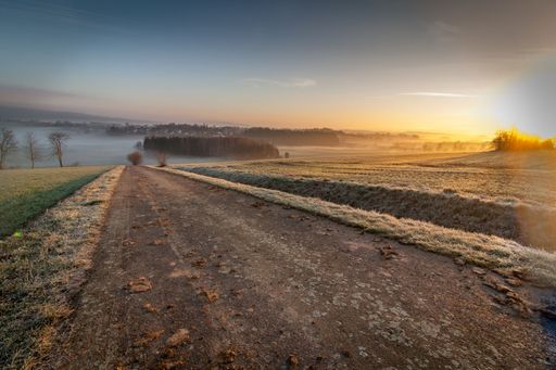 The view of a soil road before the steam-covered lake under the blue morning sky