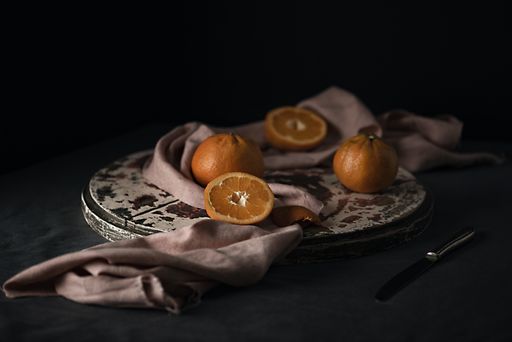 A closeup still life of mandarin orange fruits on a weathered piece of a wood tray with a towel and knife on a rustic surface