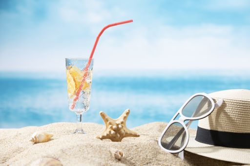 A hat, sunglasses, a starfish and a glass of lemon water on the sand on an ocean background