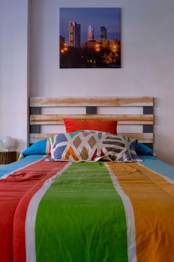 A vertical shot of a colorful bed in the room with a picture of skyscrapers hanging on the wall