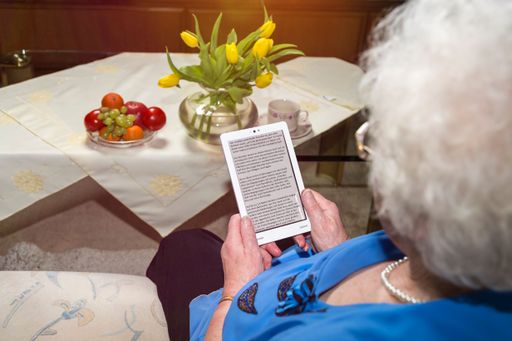 An overhead closeup shot of an old woman reading a book on a white ebook