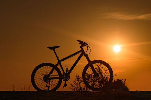 A hardtail mountain bike is photographed on top of a hill with the sun setting in the background.