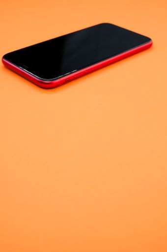 A vertical shot of a red smartphone isolated on an orange background