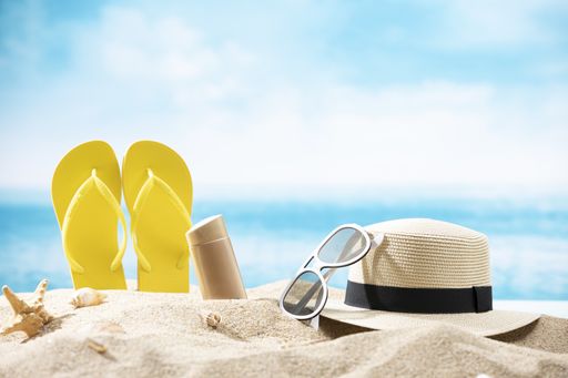 A bottle of beer, slippers, a hat, sunglasses and a starfish on the sand on the ocean background