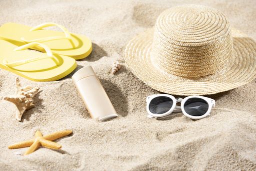 A pair of sunglasses, hat, slippers and a starfish on the sand on the beach