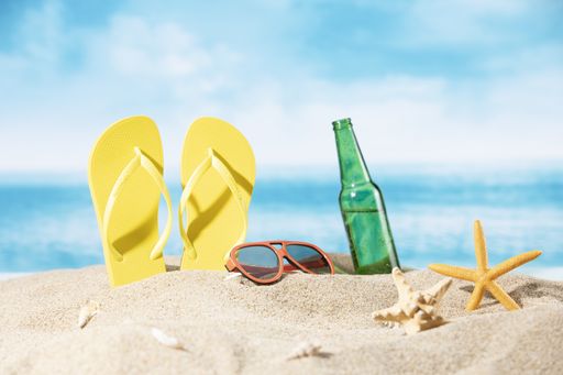 A bottle of beer, slippers, sunglasses and a starfish on the sand on the ocean background