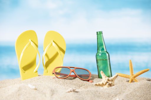 A bottle of beer, slippers, sunglasses and a starfish on the sand on the ocean background