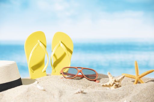 A hat, slippers and sunglasses in the sand with starfishes on the ocean and palm tree background